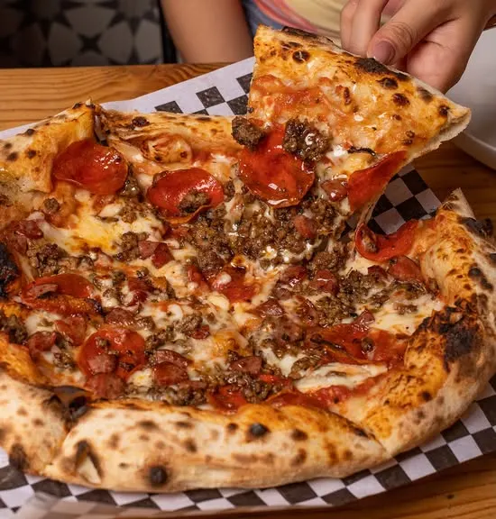 Una pizza de Caja Negra sobre su papel a cuadros, sacando una rebanada