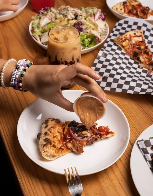 Una rebanada de pizza que se moja en aderezo, con ensalada al fondo